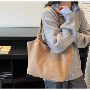 Close-up of brown suede tote bag featuring gold metal hardware and adjustable shoulder strap