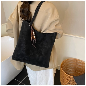 Detail view of a black suede tote bag with vintage beaded tassel and long shoulder strap