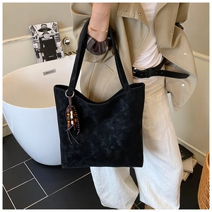 Detail of black suede tote bag with wooden bead tassel charm on a model