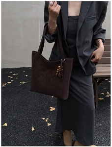 Detail of dark brown suede tote bag with ethnic beaded tassel charm in autumn outdoor setting