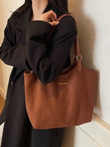 Minimalist brown suede tote bag with metal detail shown on a model in professional attire