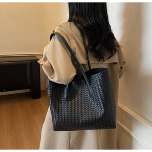 Grand sac cabas tressé noir porté par un mannequin en trench-coat beige minimaliste