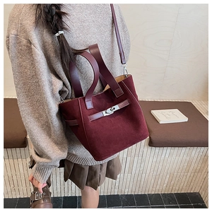 Detail of burgundy suede bucket bag with metal buckle strap and soft top handles