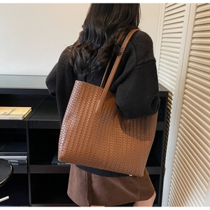 Détail macro du grand sac cabas en cuir tressé marron porté par un mannequin à l'épaule