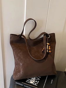 Large dark brown suede tote bag with beaded tassel detail against a white wall