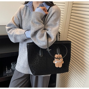 Detail of black leopard embossed tote bag with leather handles and bear charm