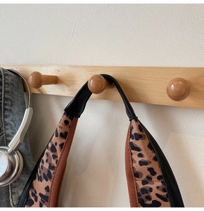 Dettaglio della tracolla leopardata su borsa hobo appesa a un gancio di legno