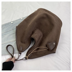 Detail shot of a dark brown suede crescent tote bag with leather piping on white fabric