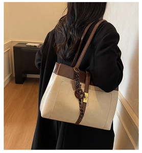 Détail d'un sac cabas contrasté avec un fermoir tournant doré et un pendentif nœud en cuir