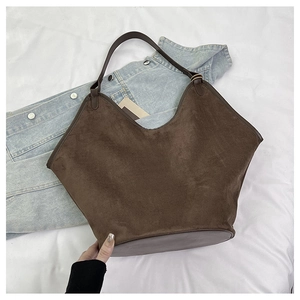 Detail of large dark brown tote bag in matte suede and leather texture on a casual bed