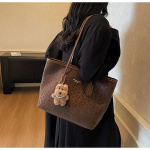 Detail of leopard print tote bag with plush bear charm and slender shoulder straps