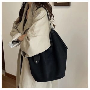 Detail view of large black leather tote bag with flap and metal snap button closure