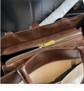 Détail d'une fermeture éclair dorée lisse sur un grand sac cabas marron foncé