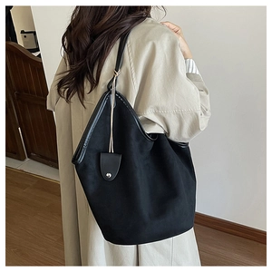 Side view of large black bucket tote bag with leather trim on model in beige coat