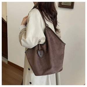 Detail of a large brown suede hobo tote bag featuring a leather charm for a vintage look