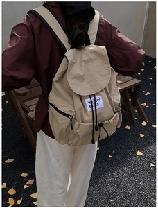 Vue détaillée du sac à dos beige à cordon avec rabat et écusson logo tissé