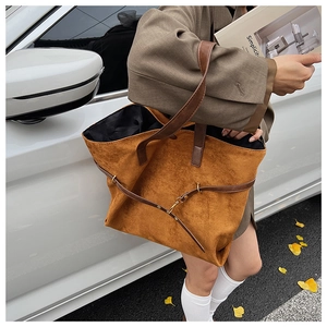 Detailed view of brown suede tote bag featuring leather handles and buckle strap