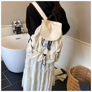 Détail du sac à dos en toile blanc cassé avec fermeture à cordon et poche latérale zippée