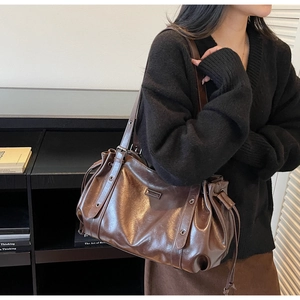 Detail of a deep brown glossy leather tote bag featuring drawstring pleats and metal eyelets