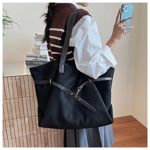 Detail view of large black tote bag with decorative leather straps and gold metal buckle
