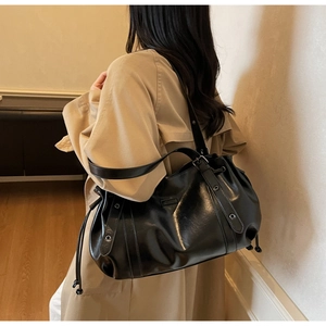 Detail of a black shiny tote bag with drawstring texture and rivet straps on a model