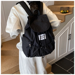 Détail du sac à dos noir en nylon avec cordon de serrage, rabat et étiquette tissée