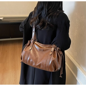 Detail of brown oil-wax leather shoulder bag with adjustable eyelet strap and side drawstring