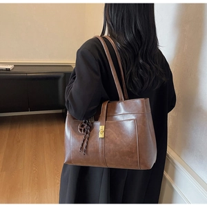 Detail of a large dark brown leather tote bag with a gold buckle and braided ornament