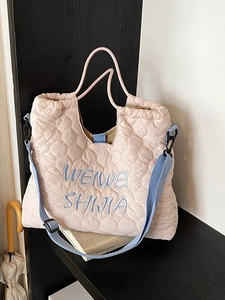 Sac fourre-tout matelassé rose avec broderie bleue et bandoulière contrastée sur un présentoir