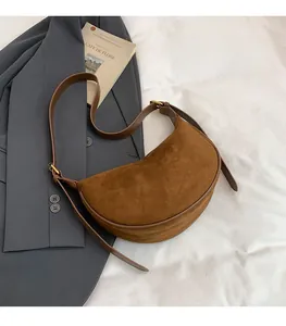 Detailansicht einer dunkelbraunen Wildleder-Halbmondtasche mit goldener Schnalle auf Stoff