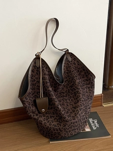 Large leopard print tote bag with brown leather handles and side tassels on wood floor