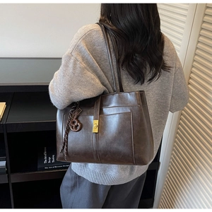 Detail of dark brown tote bag with glossy leather texture and gold square buckle detail