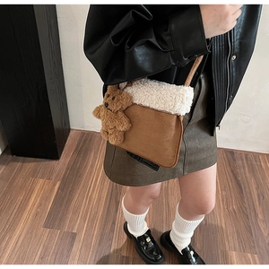 Close-up of brown suede bucket bag with white faux fur trim and cute plush bear charm