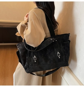 Detail of black matte tote bag featuring silver metal buckles and wide shoulder strap
