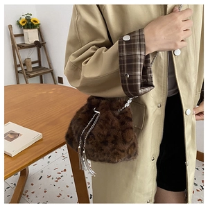 Détail du sac seau en peluche léopard avec chaîne en métal et pompon sur table en bois