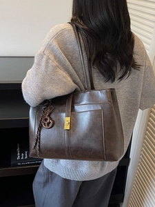 Large dark brown tote bag with gold buckle on shoulder of model in cozy setting