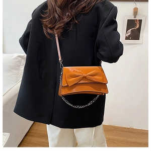 Détail du sac à bandoulière en cuir verni jaune gingembre avec nœud et chaîne argent