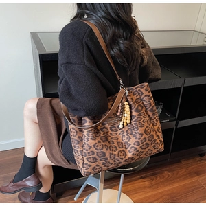 Detail of leopard print tote bag with brown leather straps and beaded wooden charm