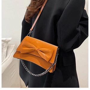 Détail d'un sac bandoulière orange avec nœud et chaîne argentée sur mannequin en tailleur