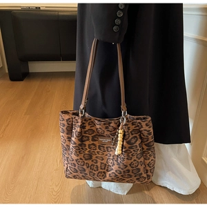 Detail of leopard print tote bag featuring brown leather straps and beaded charm accessory
