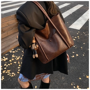 Detail of dark brown leather bucket bag with a cute rabbit charm in autumn city setting