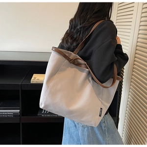 Detailed view of canvas tote bag with brown leather trim and brand label in room