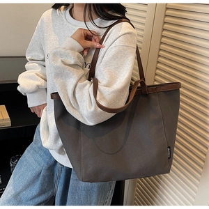 Detail of grey canvas tote bag with brown leather straps and branded woven label
