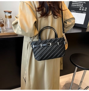 Detail of woven texture Boston bag with leather strap and silver buckle on a trench coat