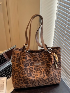 Leopard print tote bag with brown leather handles and wooden bead charm in sunlight