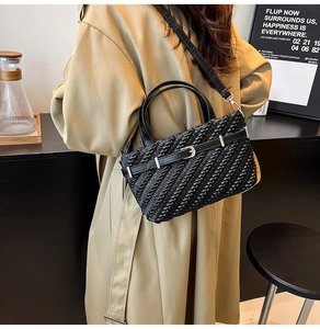 Detail of black woven tote bag with silver buckle worn with a beige trench coat