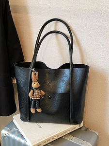 Black vintage leather tote bag with a cute rabbit charm on a stylish commuter background
