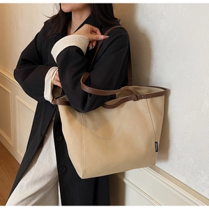 Detail of beige canvas tote bag with brown leather shoulder straps and woven side label