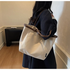 Detail of canvas tote bag with contrast leather trim and logo label on model's shoulder