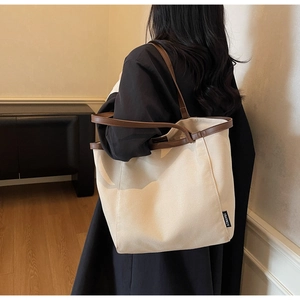 Side view of beige canvas tote bag with brown leather trim and shoulder strap on model